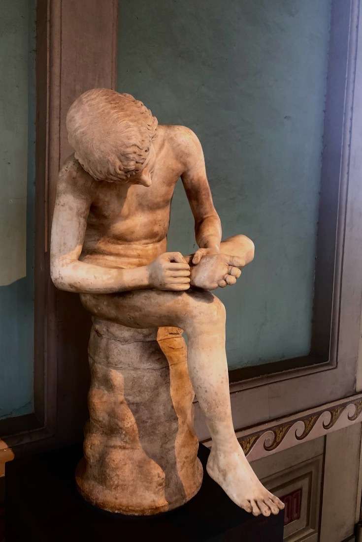 Sculpture of naked man picking something from his foot at museum in Florence